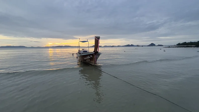 A longtail boat moored off Klong Muang Beach at sunset