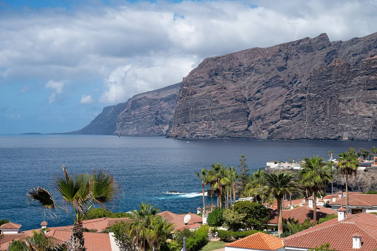 The cliffs of Los Gigantes rising above the Atlantic beside palms and coastal buildings